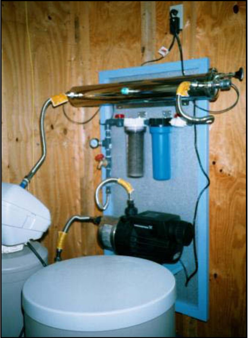 Foto de una instalación de tratamiento en pared: bomba bajo demanda, filtro de cartucho de fibra, filtro de carbón activado y lámpara ultravioleta arriba.